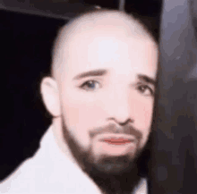 a close up of a bald man with a beard wearing a white shirt .