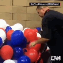 a man is standing in front of a bunch of red white and blue balloons with a cnn logo in the corner