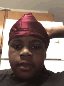 a young man wearing a maroon head scarf is looking at the camera