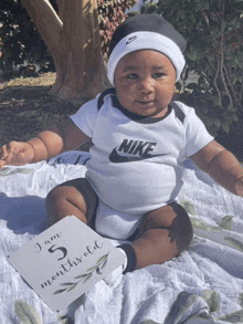 a baby is wearing a nike outfit and holding a card that says i am 5 months old