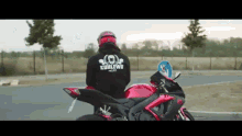 a man is sitting on a red motorcycle wearing a helmet and a hoodie that says konlewu on the back