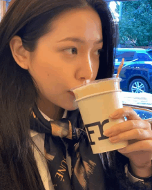 a woman drinking from a cup that has the letter e on it