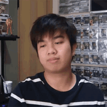 a young man in a black and white striped shirt is sitting in front of a wall filled with funko pop figures .