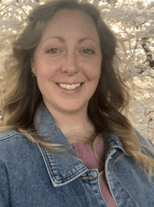 a woman wearing a denim jacket is smiling in front of a tree