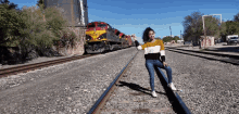 a woman sits on a train track in front of a train that says bnsf on the front of it