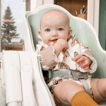 a baby is sitting in a high chair with a rainbow shirt on