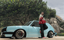 a man standing next to a blue car with a tree in the background