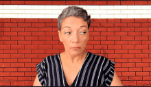 a woman wearing a striped shirt is standing in front of a brick wall