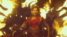 a woman in a red and gold costume is standing in front of a fire