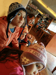 a boy wearing a hat that says cusco sits next to two other children