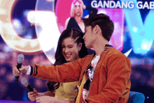 a man and a woman are taking a selfie in front of a sign that says gandang gab