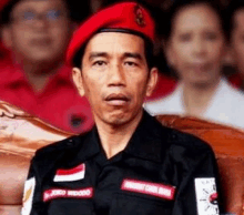 a man wearing a red beret and a black shirt is sitting in a chair .