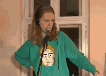 a woman singing into a microphone wearing headphones and a green sweatshirt with a pixelated face on it