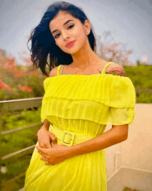 a woman in a bright yellow off the shoulder dress is standing on a balcony