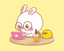 a cartoon rabbit is sitting at a table with a laptop and a drink .