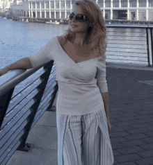 a woman wearing sunglasses leans against a railing overlooking the water