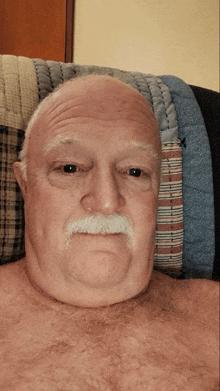 a shirtless man with a mustache is sitting on a couch