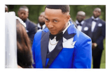 a man in a blue tuxedo is standing in front of a bride and her groomsmen