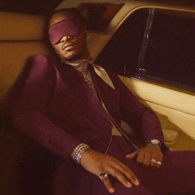 a man in a purple suit is sitting in a car wearing a blindfold