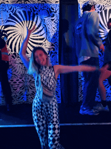 a woman in a black and white outfit is dancing in front of a wall with a swirl pattern