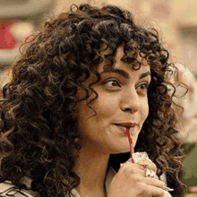 a woman with curly hair is drinking through a straw from a cup .