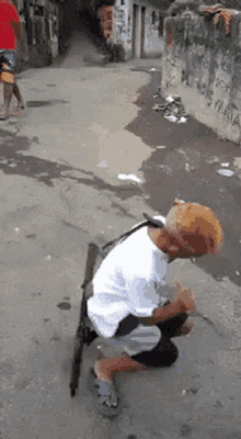 a man in a white shirt is kneeling down with a gun around his neck