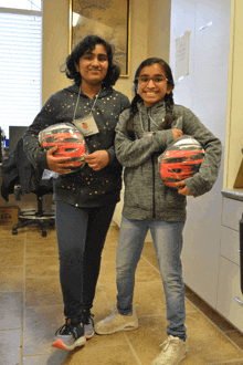 two girls are holding helmets and one has a name tag on