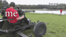 a man in a red shirt is sitting in front of a cannon with the word me on his back