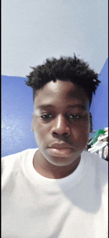 a young man in a white shirt looks at the camera with a blue wall in the background