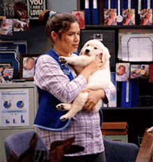 a woman in a blue vest is holding a puppy in front of a sign that says you are loved