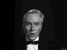 a black and white photo of a man in a tuxedo with his mouth open