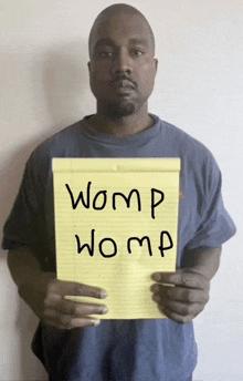 a man in a blue shirt is holding a yellow notepad with the words womp womp written on it