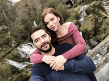 a man and a woman are posing for a picture in front of a waterfall