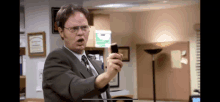 a man in a suit and tie is holding a cell phone in front of a green exit sign