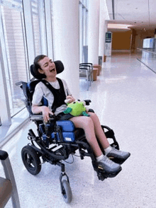 a young boy in a wheelchair is holding a stuffed frog in a hallway .