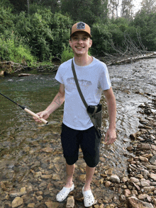 a man holding a fishing rod in a river wearing a t-shirt that says hurley on it