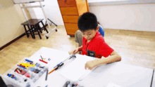 a young boy in a red shirt sits at a table with a box of lego blocks