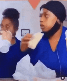 two women are sitting at a table eating food and drinking milk . one of the women is wearing a mask .