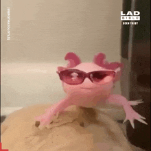 a pink axolotl wearing sunglasses is sitting on top of a piece of wood .