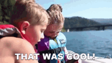 two young boys are sitting on a boat looking at a cell phone with the words that was cool written on the bottom .