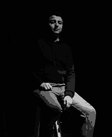 a man in a black hoodie is sitting on a stool in the dark