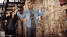 a man and a woman are standing in front of a brick wall with the nbc logo on the bottom right