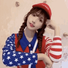 a woman wearing a red hat and an american flag shirt is flexing her arm .