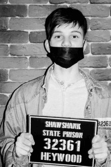 a man wearing a black mask holds up a shawshank state prison sign