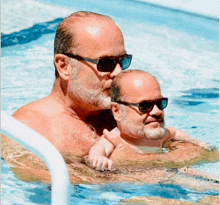 a man holding a baby in a pool wearing sunglasses