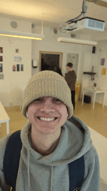 a man wearing a beanie and a grey hoodie smiles for the camera