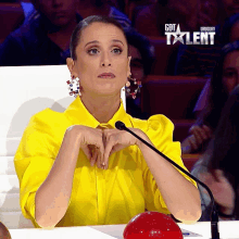 a woman in a yellow shirt sits in front of a microphone with the words got talent uruguay on the bottom