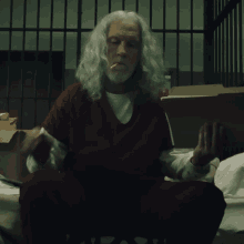 a man with long white hair is sitting in a prison cell