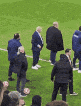 a group of men are standing on a soccer field and one of them is wearing a blue jacket that says ' united '