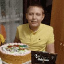 a boy in a yellow shirt is sitting at a table with a birthday cake .